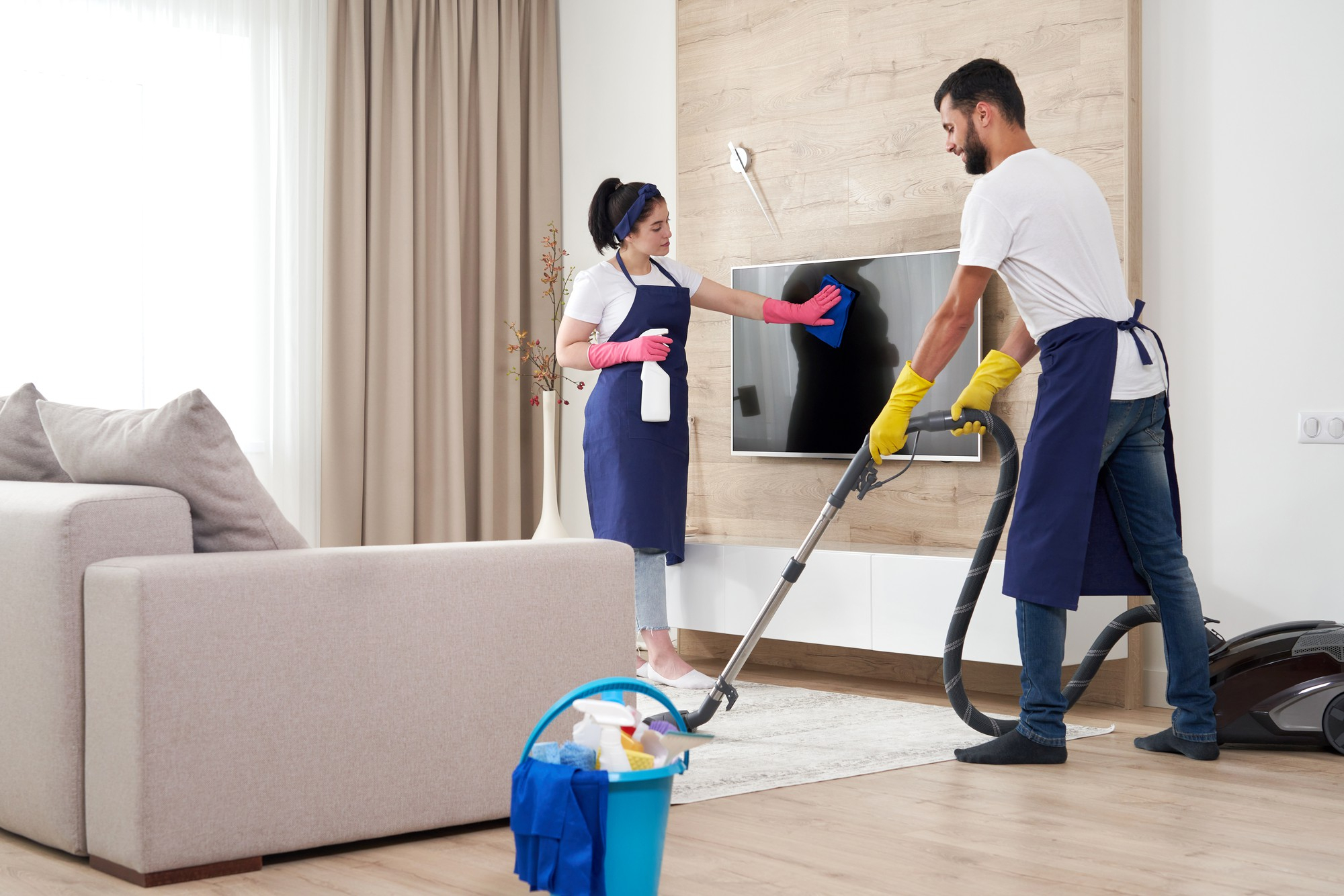 Cleaner Dallas team performing living room cleaning with vacuuming and TV screen wiping.