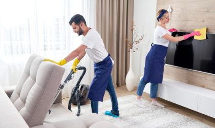 Professional Dallas cleaners vacuuming sofa and wiping TV during home cleaning service.