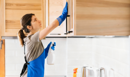Professional kitchen cleaning service in Dallas wiping wooden cabinets with cleaning spray